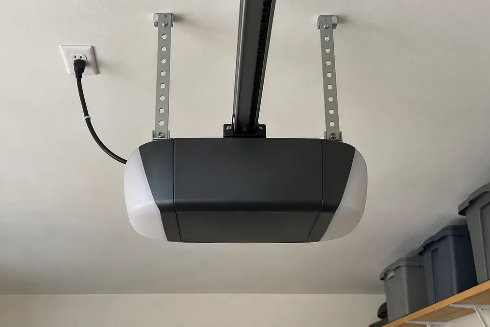 New belt-drive garage door opener hanging from ceiling straps and plugged into a ceiling outlet