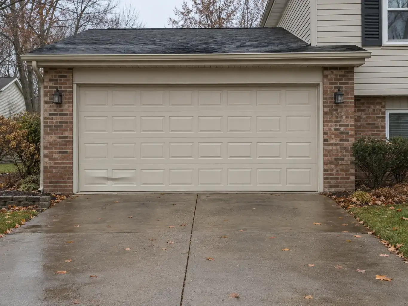 Closed almond two-car garage door on a brick house, dented across two bottom-section panels