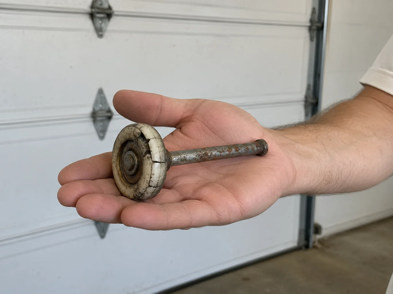 Open palm holding a worn, cracked nylon garage door roller with a rusty steel stem