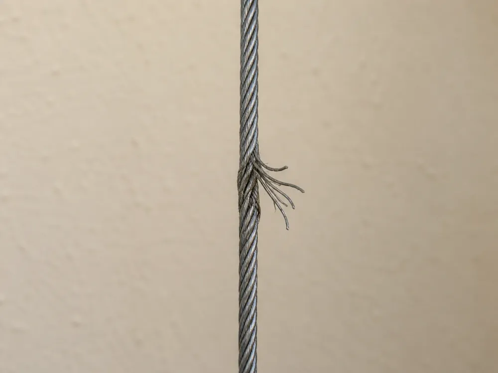 Close-up of a frayed garage door lift cable with broken steel wires splaying out