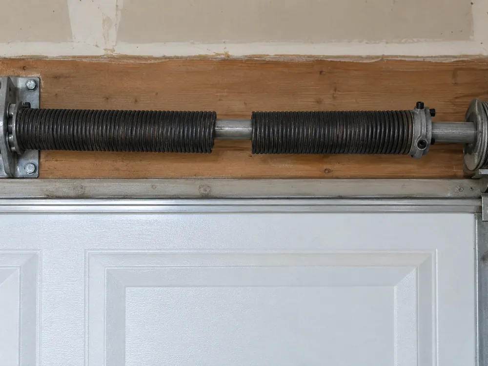 Snapped torsion spring with a clear gap between its coils above a closed garage door