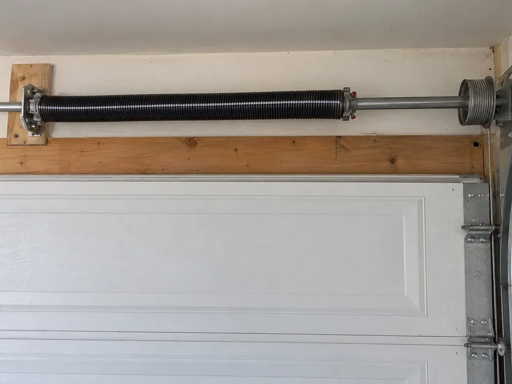 New torsion spring with a paint stripe above a closed garage door, next to the cable drum