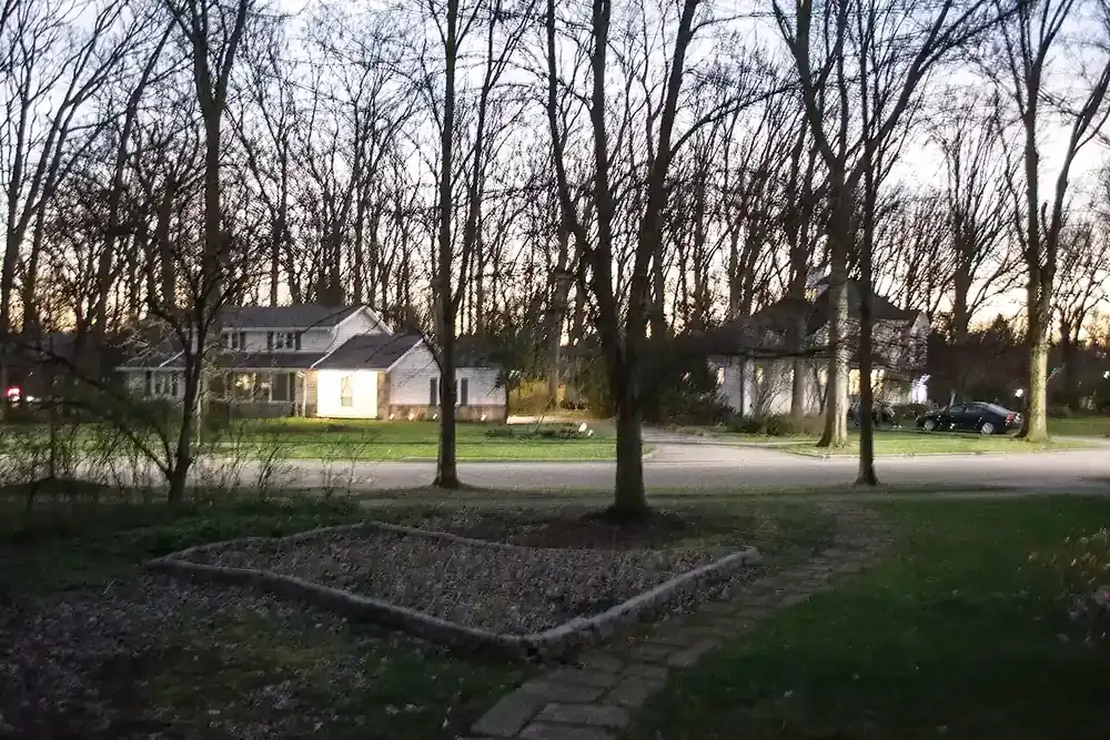 Lit white house across a wooded front yard at dusk in Cleveland Heights