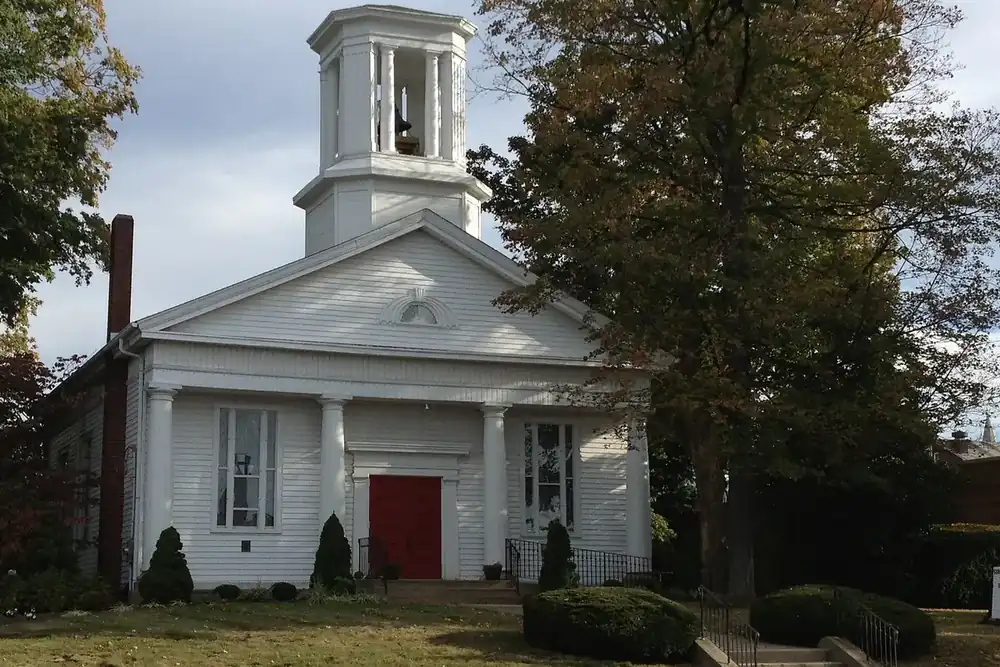 A white church with a bell tower and red doors among trees in Wadsworth, Ohio